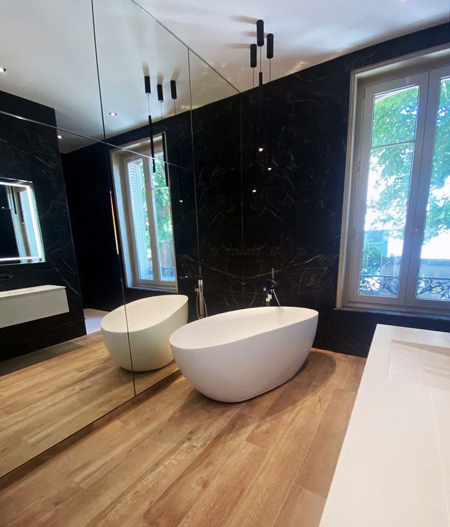 Salle de bain moderne noire et blanche avec parquet, deux baignoires en forme d'œuf, un grand miroir et des fenêtres.