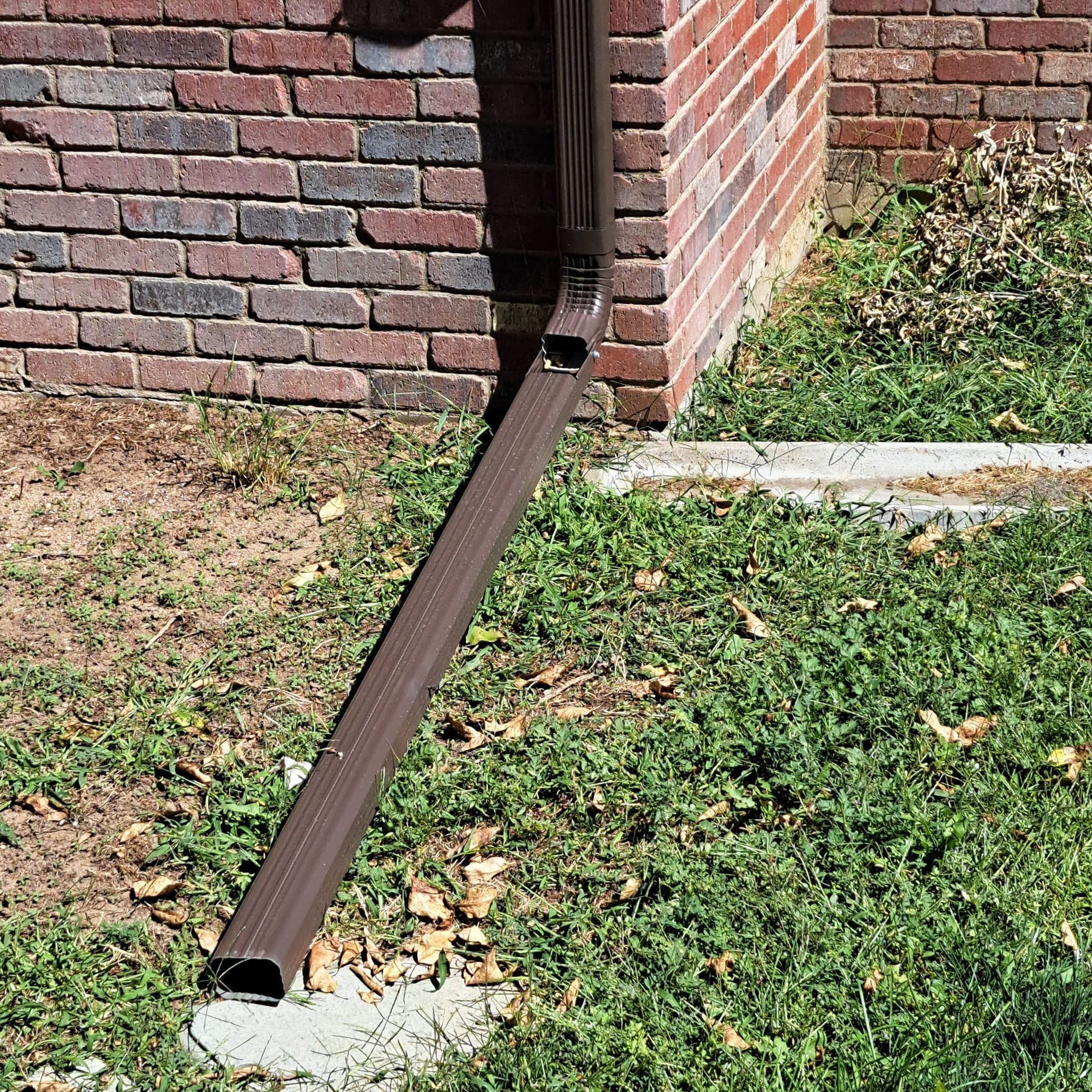 A brown gutter is sitting in the grass next to a brick wall.