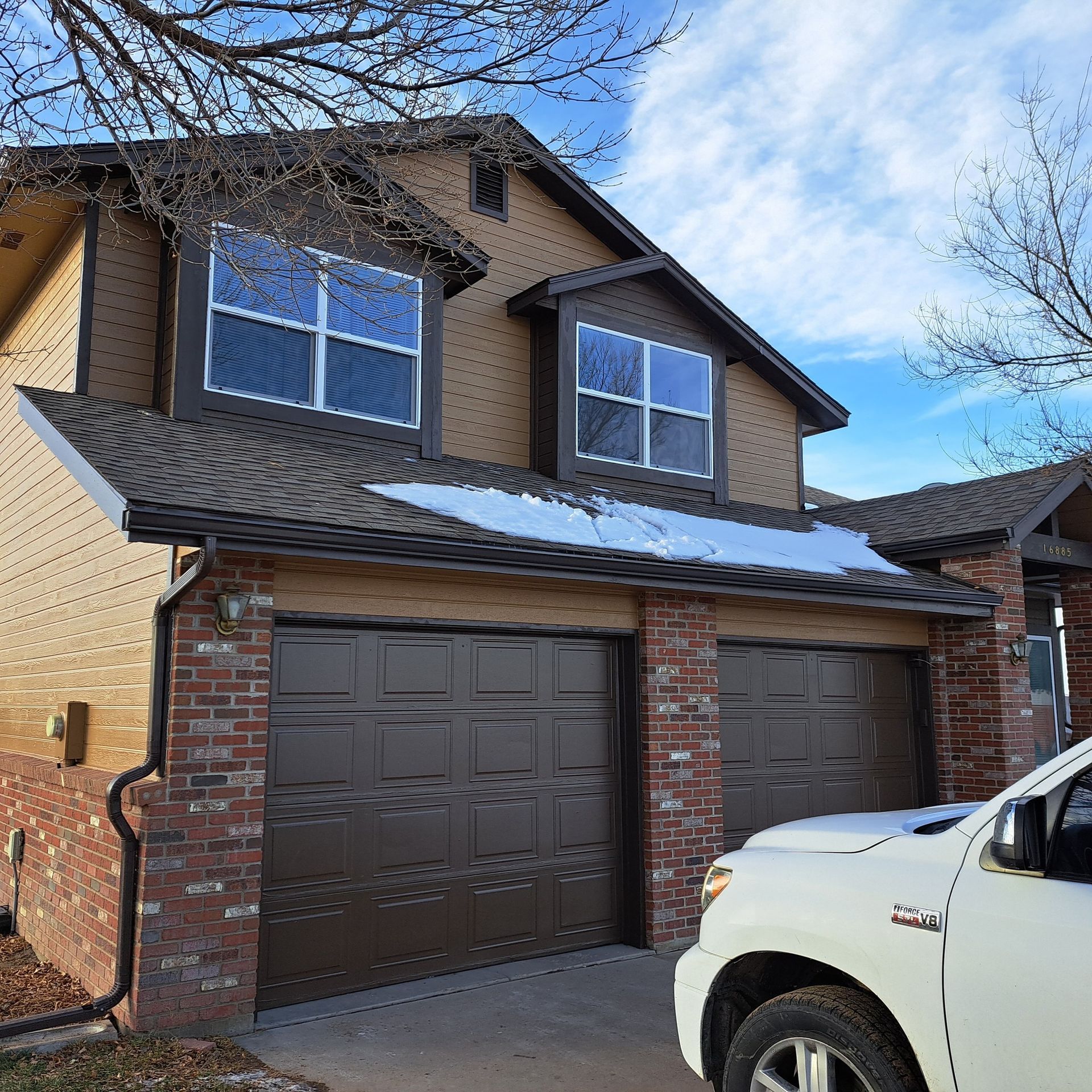 A white truck is parked in front of a house with two garage doors