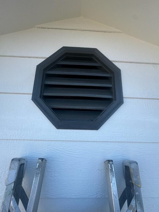 A ladder is leaning against a white wall next to a black vent