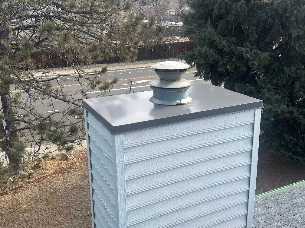 A chimney on top of a white building with a tree in the background.