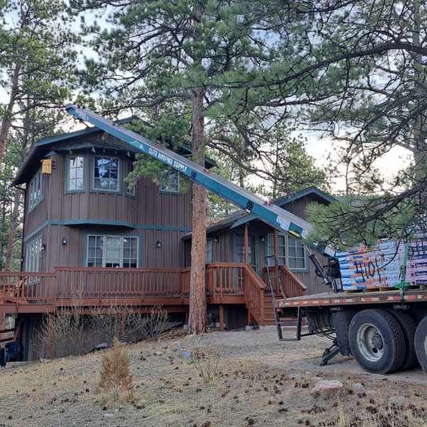 A crane is lifting a tree in front of a house.