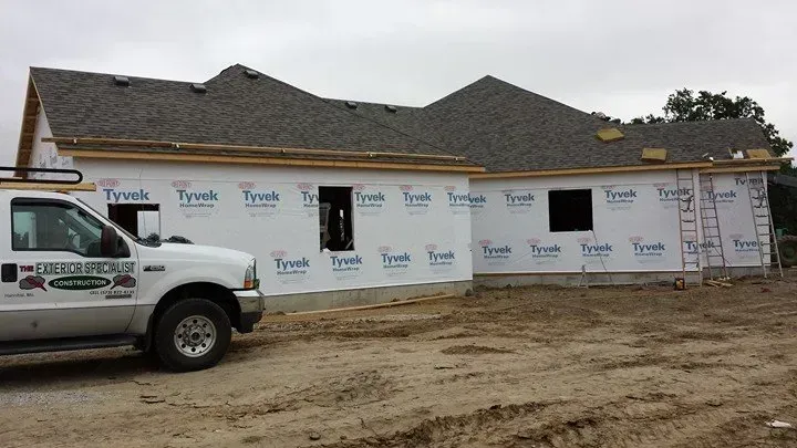 House under construction with Tyvek wrap and a white pickup truck parked beside it