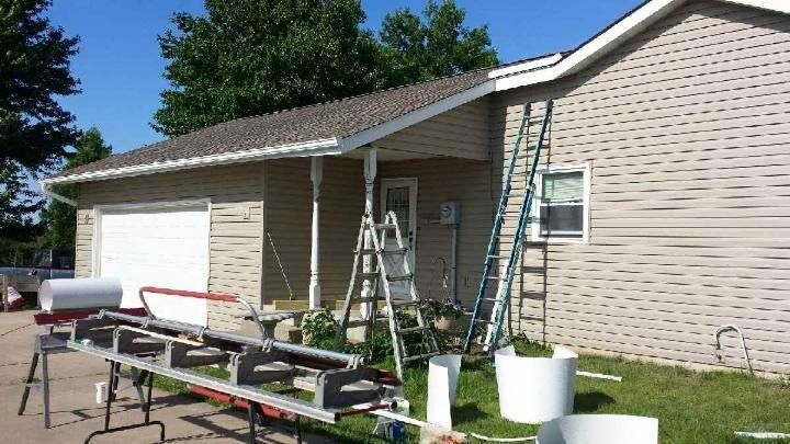 Ladders and tools outside a beige house during exterior painting or repairs, with a garage and green lawn.