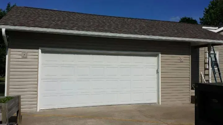 Single-car garage with a white door and tan siding under a shingled roof.