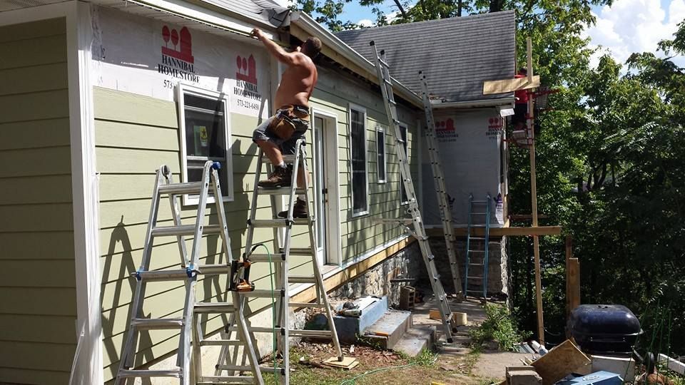 Two workers on ladders repairing the exterior roof and siding of a house