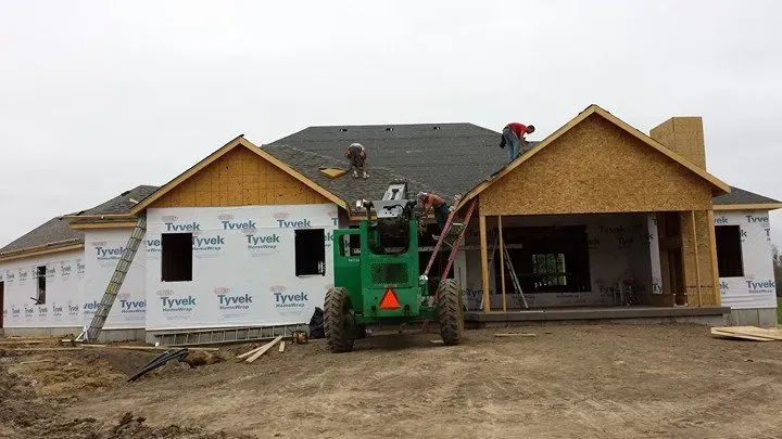 House under construction with workers on the roof and a green lift in front