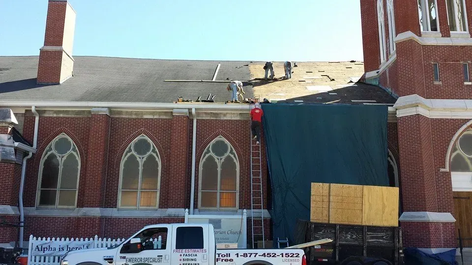 Church roof under repair with scaffolding, tarp, and construction truck in front