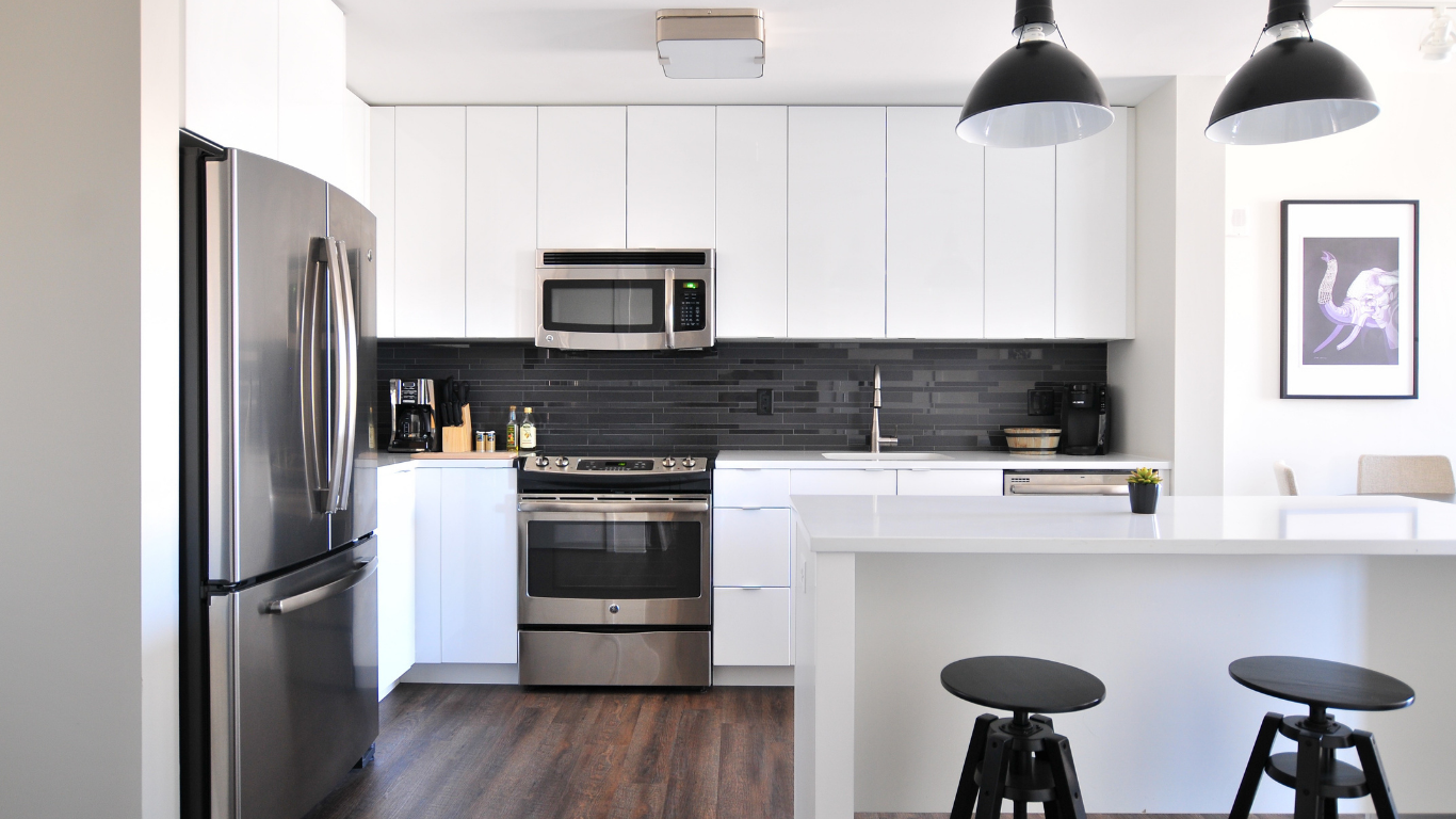 Modern white kitchen with stainless steel appliances, black backsplash, and stools at a breakfast bar.