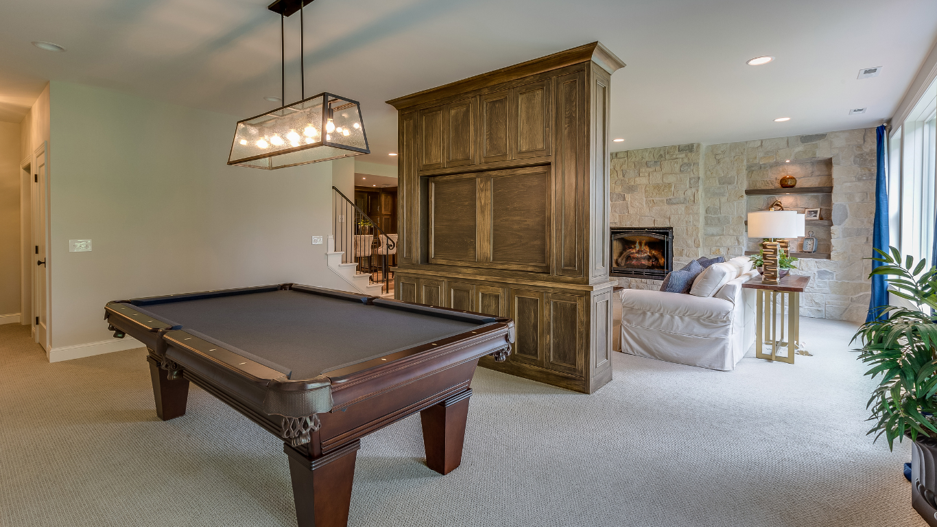 Pool table in a game room with a built-in wooden cabinet. A couch and fireplace are visible.