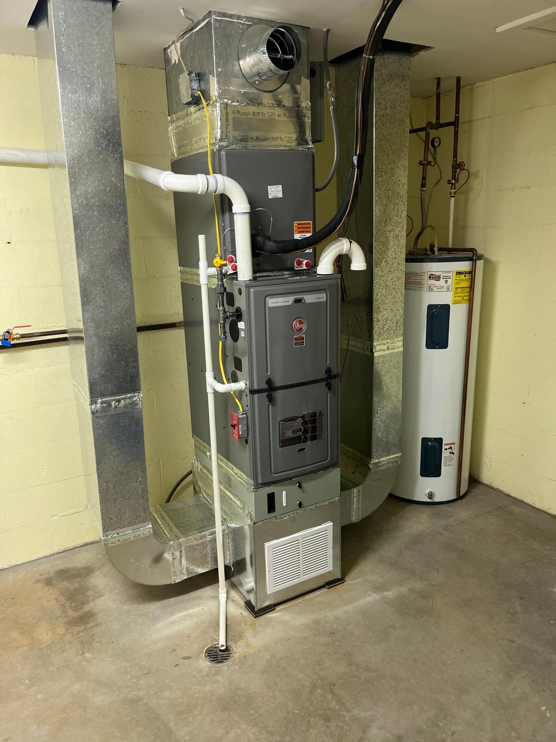 Furnace and water heater in a utility room with silver ducts, white pipes, and a yellow wall.