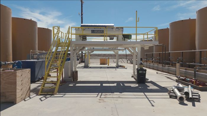 A large building with a yellow staircase is surrounded by large brown tanks