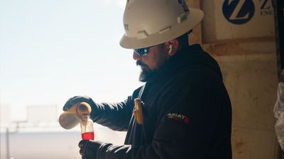 A man in a hard hat is pouring liquid into a beaker.