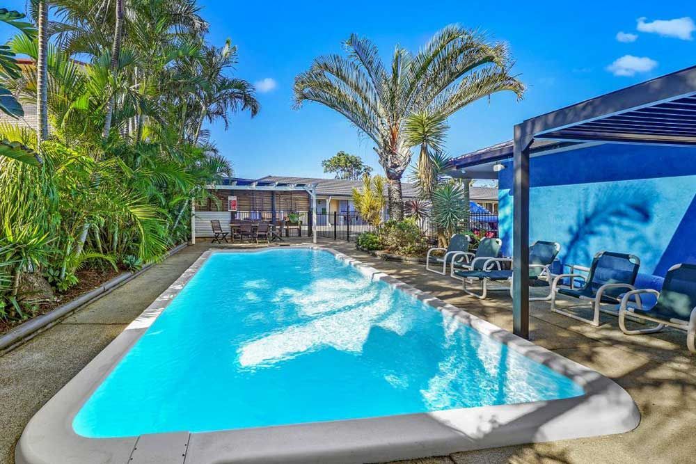A Large Swimming Pool Surrounded By Palm Trees And Chairs β Woongarra Motel In North Haven, NSW