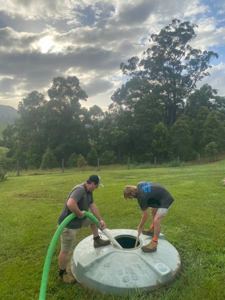 Two Men Are Working On A Septic Tank In A Grassy Field — Tweed Valley Septics & Liquid Waste Management in Bilambil, NSW