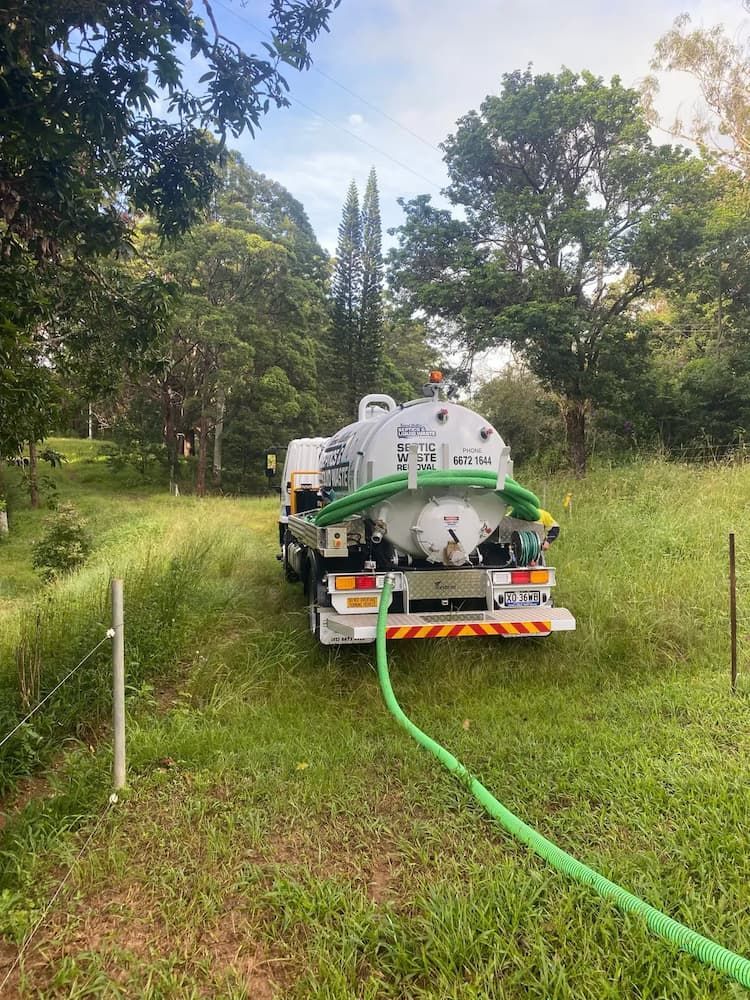 A Vacuum Truck Is Parked In A Grassy Field With A Green Hose Attached To It — Tweed Valley Septics & Liquid Waste Management in Bangalow, NSW