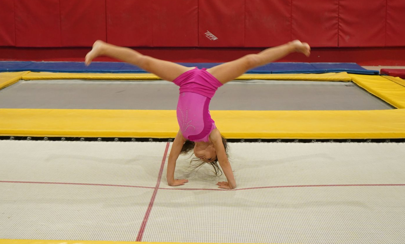 Young child jumping on a trampoline, arms raised, smiling; indoor gym setting.