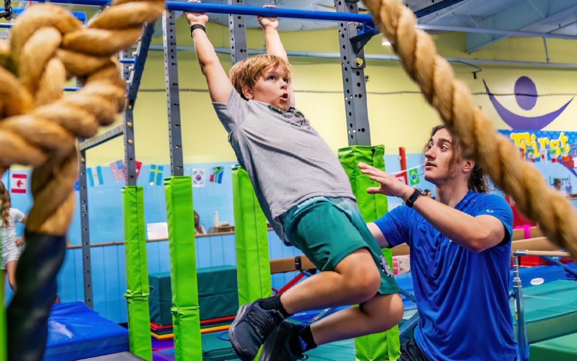 Girl in pink shorts and sports bra does the splits in a gym, two others watch.