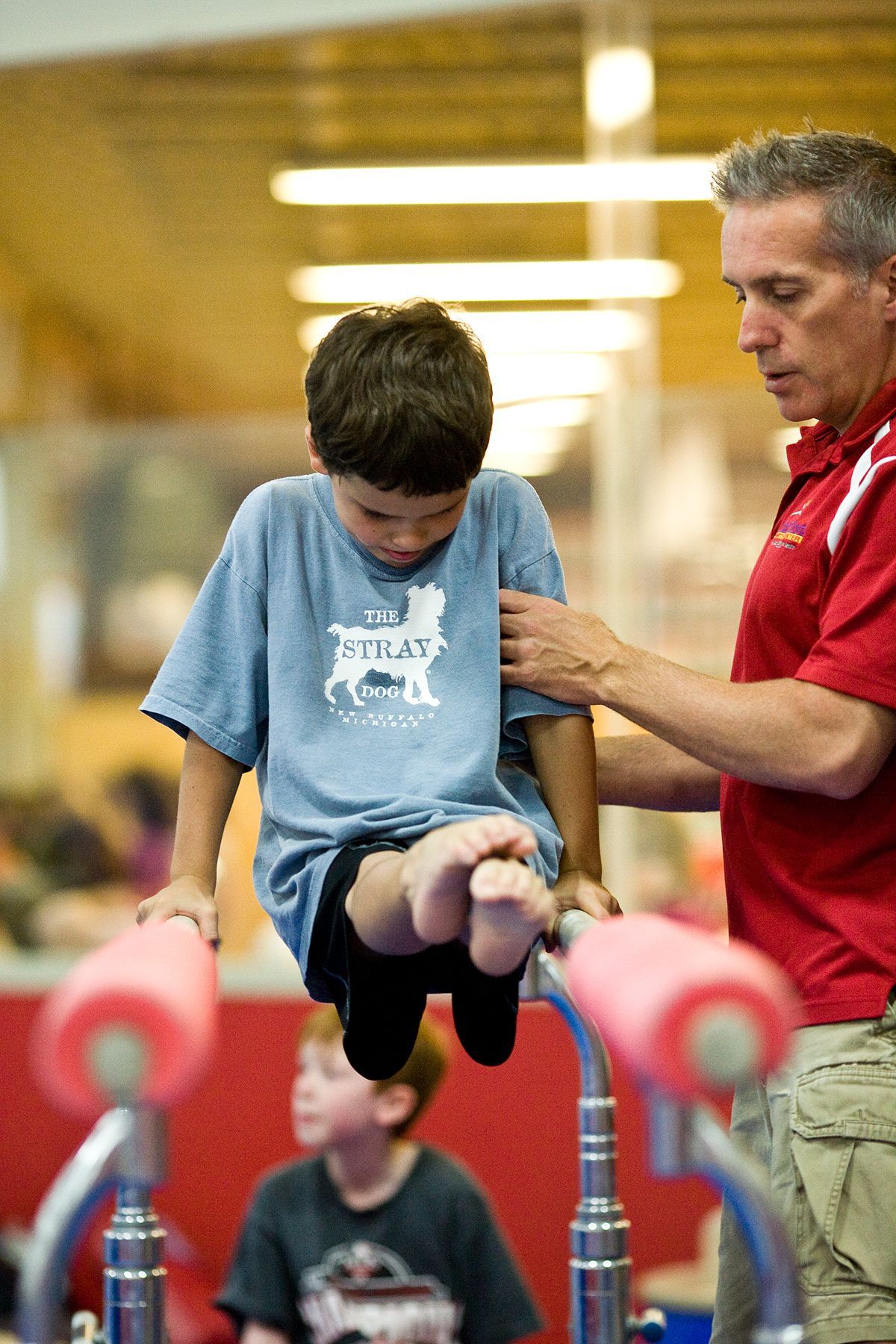 A man is helping a young boy do a trick on parallel bars.