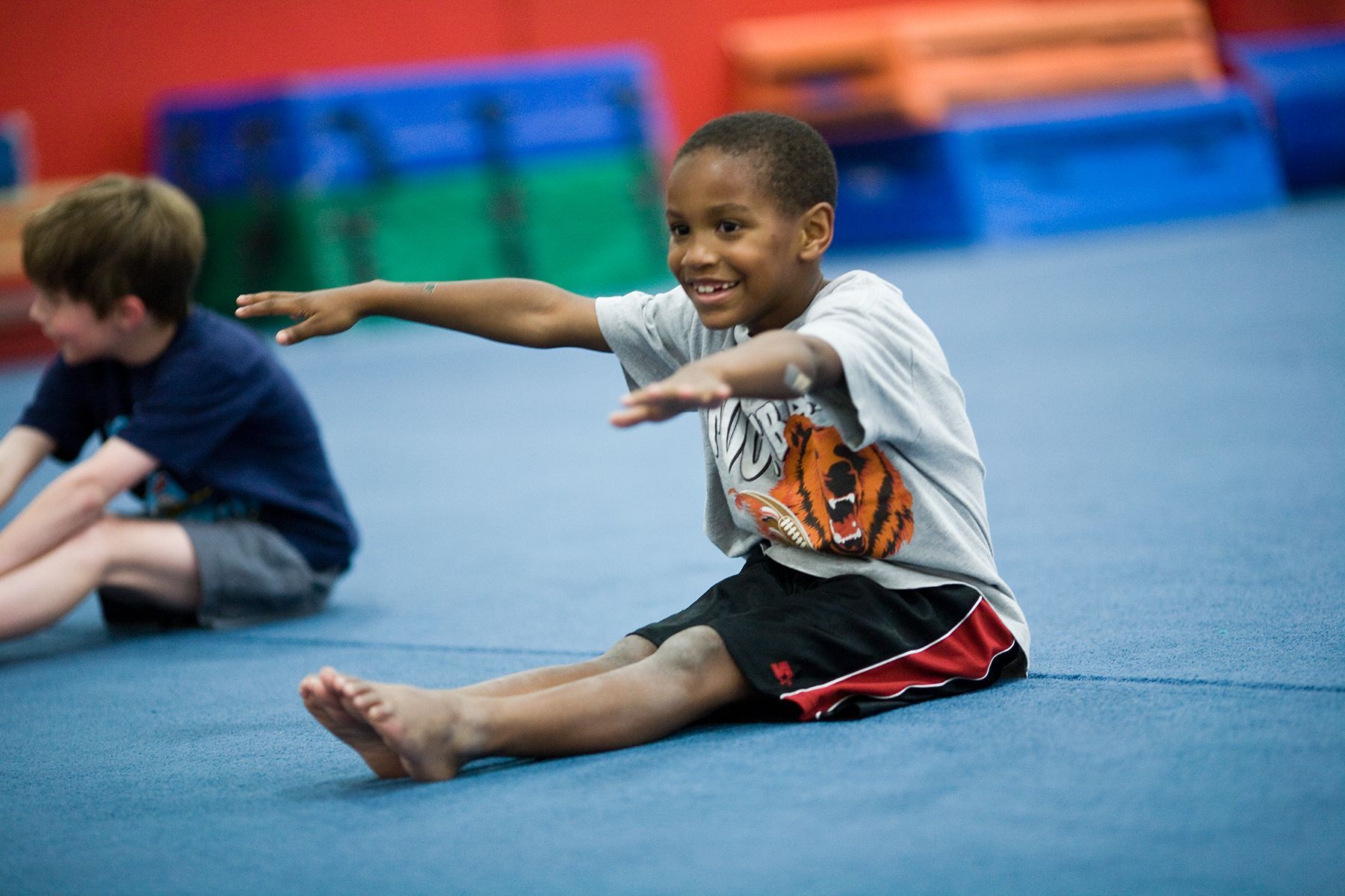A young boy is sitting on the floor stretching his legs.