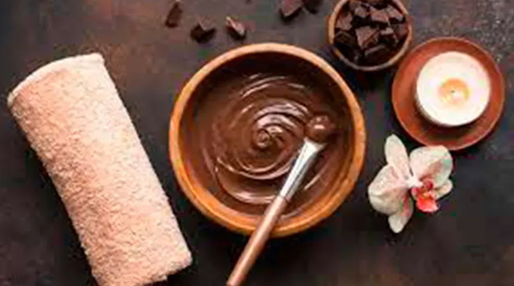 A wooden bowl filled with chocolate and a brush on a table.