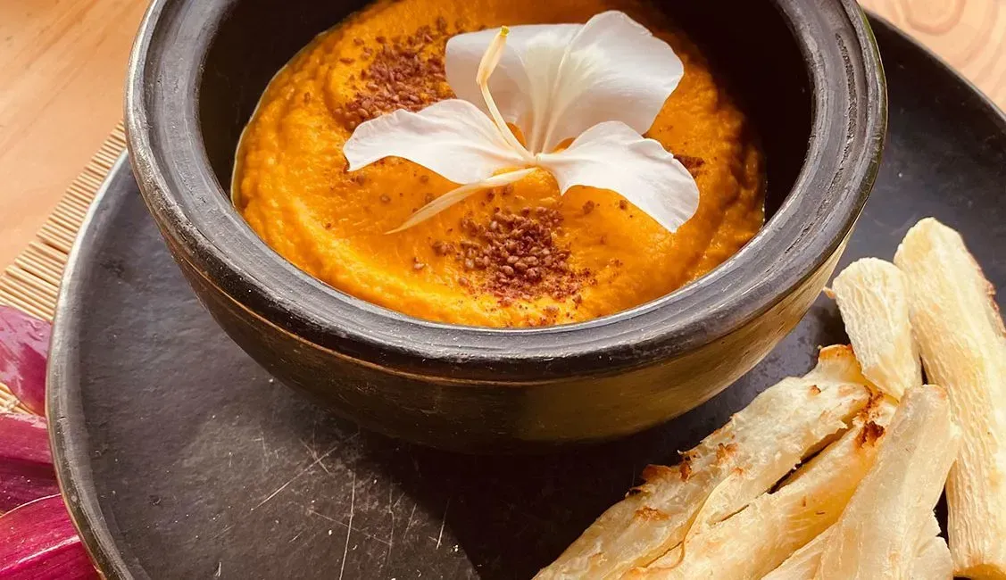 A bowl of soup with a flower on top and french fries on a plate.