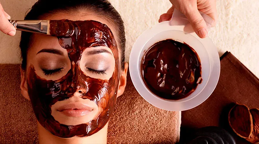 A woman is getting a chocolate mask on her face.