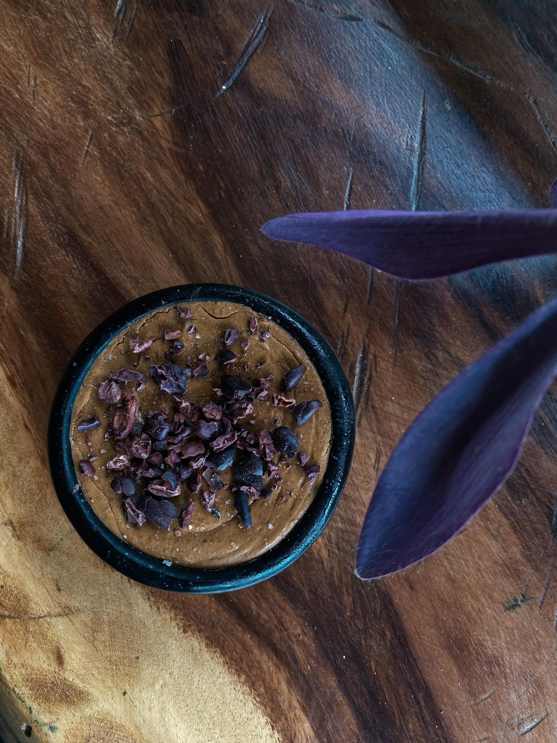 There is a bowl of food on a wooden table next to a plant.