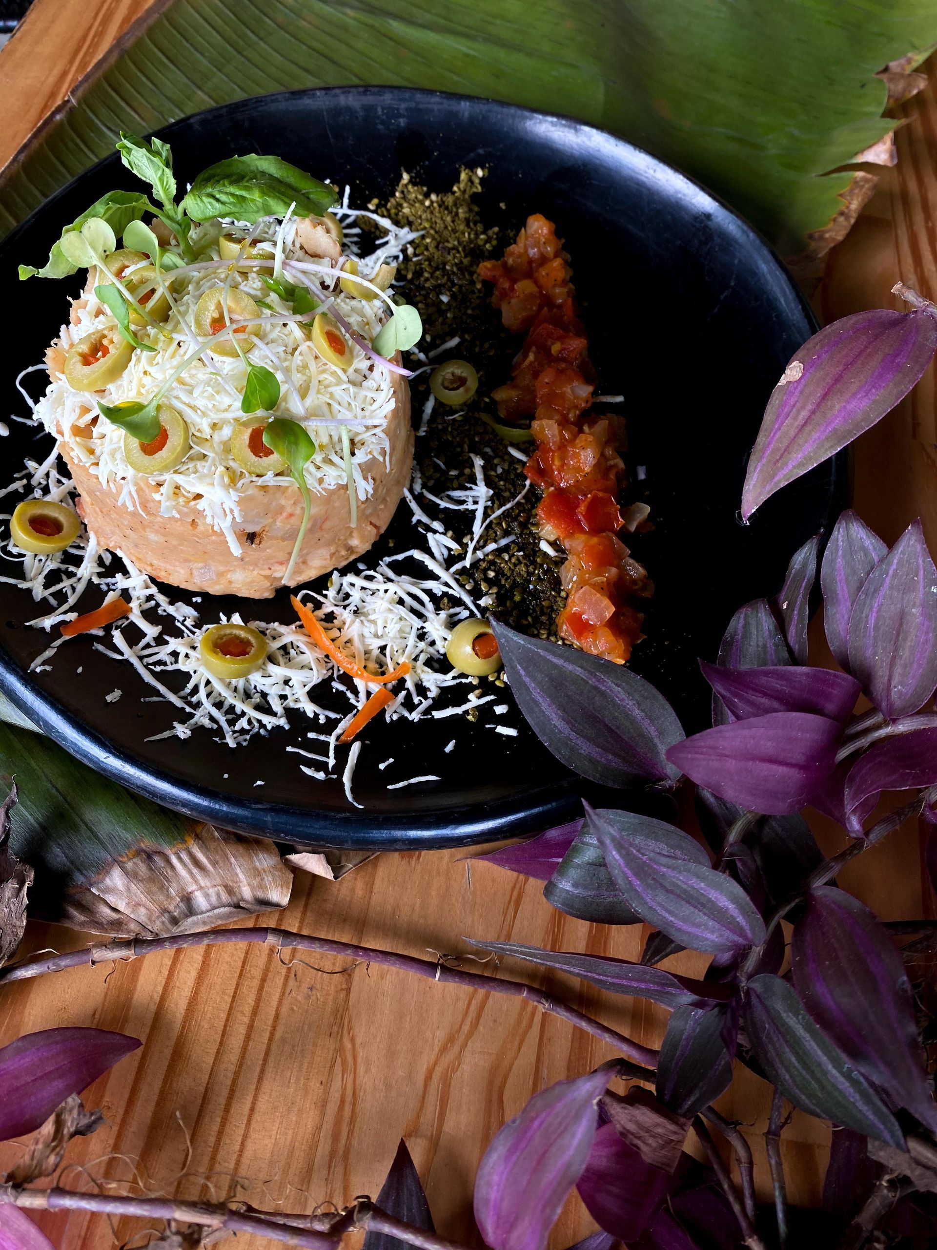 A black plate topped with a sandwich and vegetables on a wooden table.