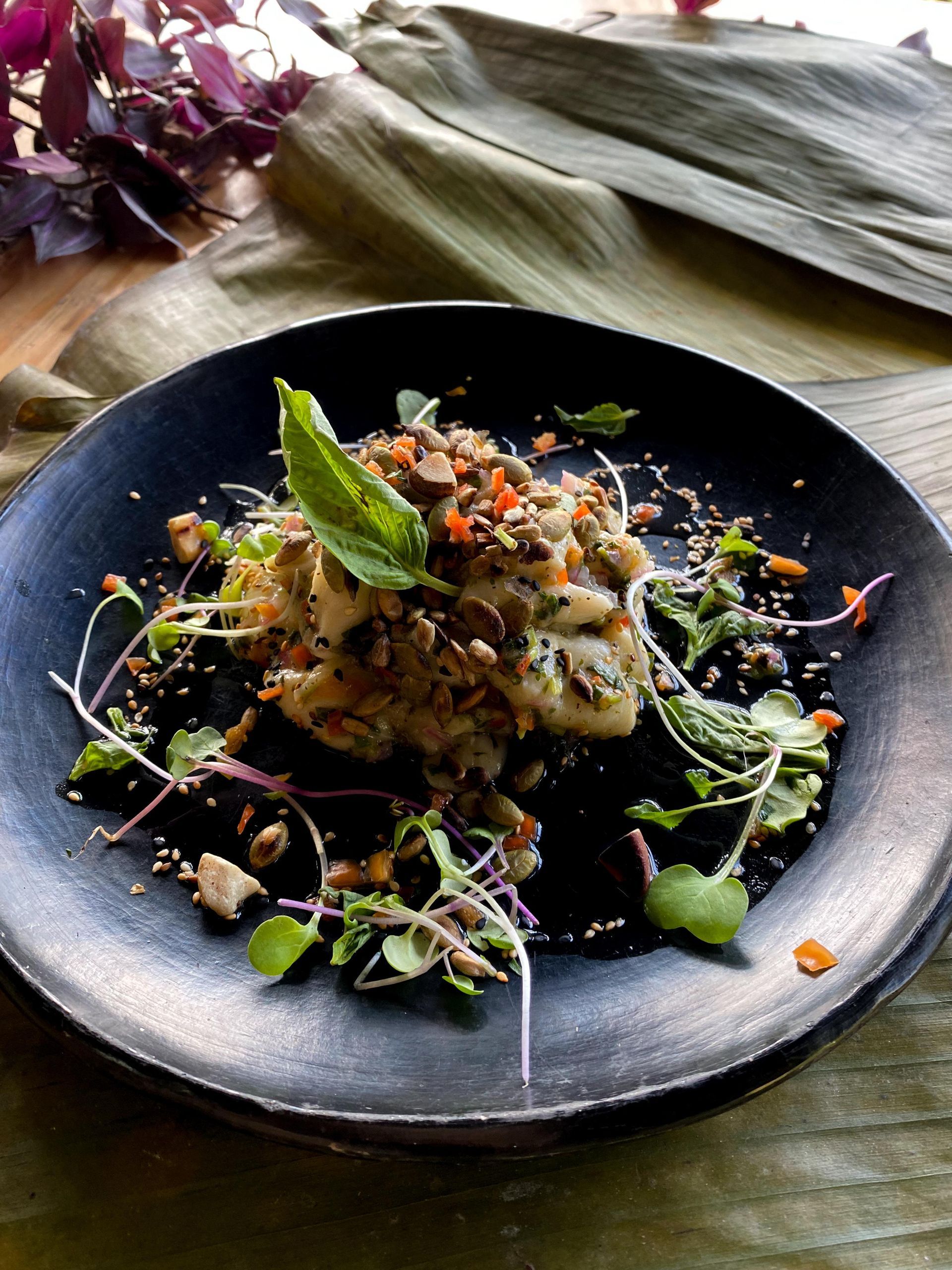 A black plate topped with a salad and vegetables on a table.
