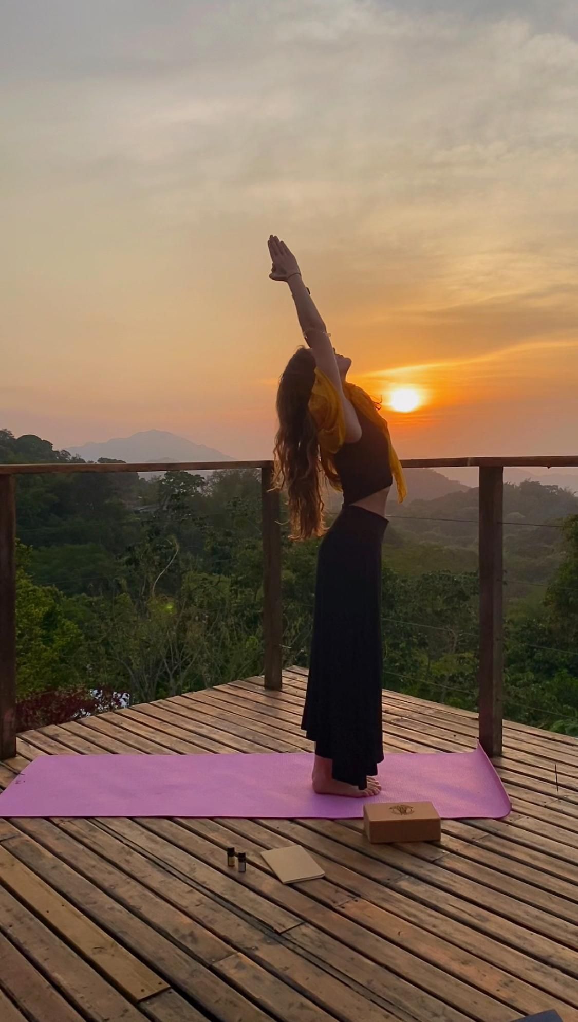 A woman is doing yoga on a wooden deck at sunset.