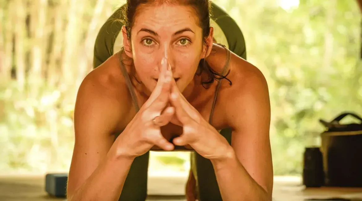 A woman is sitting on a yoga mat with her hands on her face.