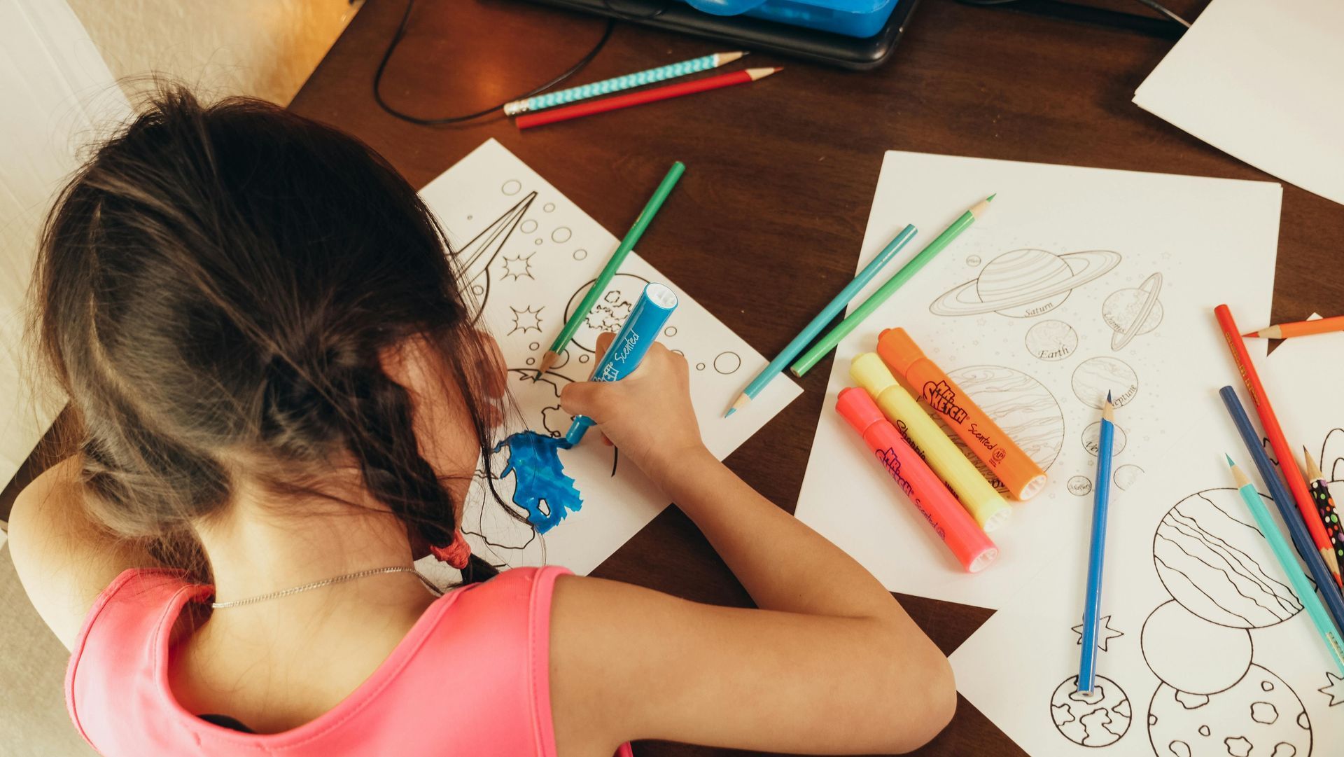 A little girl is sitting at a table drawing with markers and pencils.
