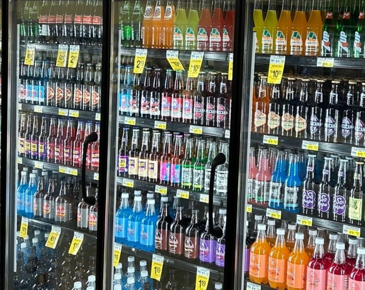 A grocery store refrigerator filled with bottles and cans of soda.