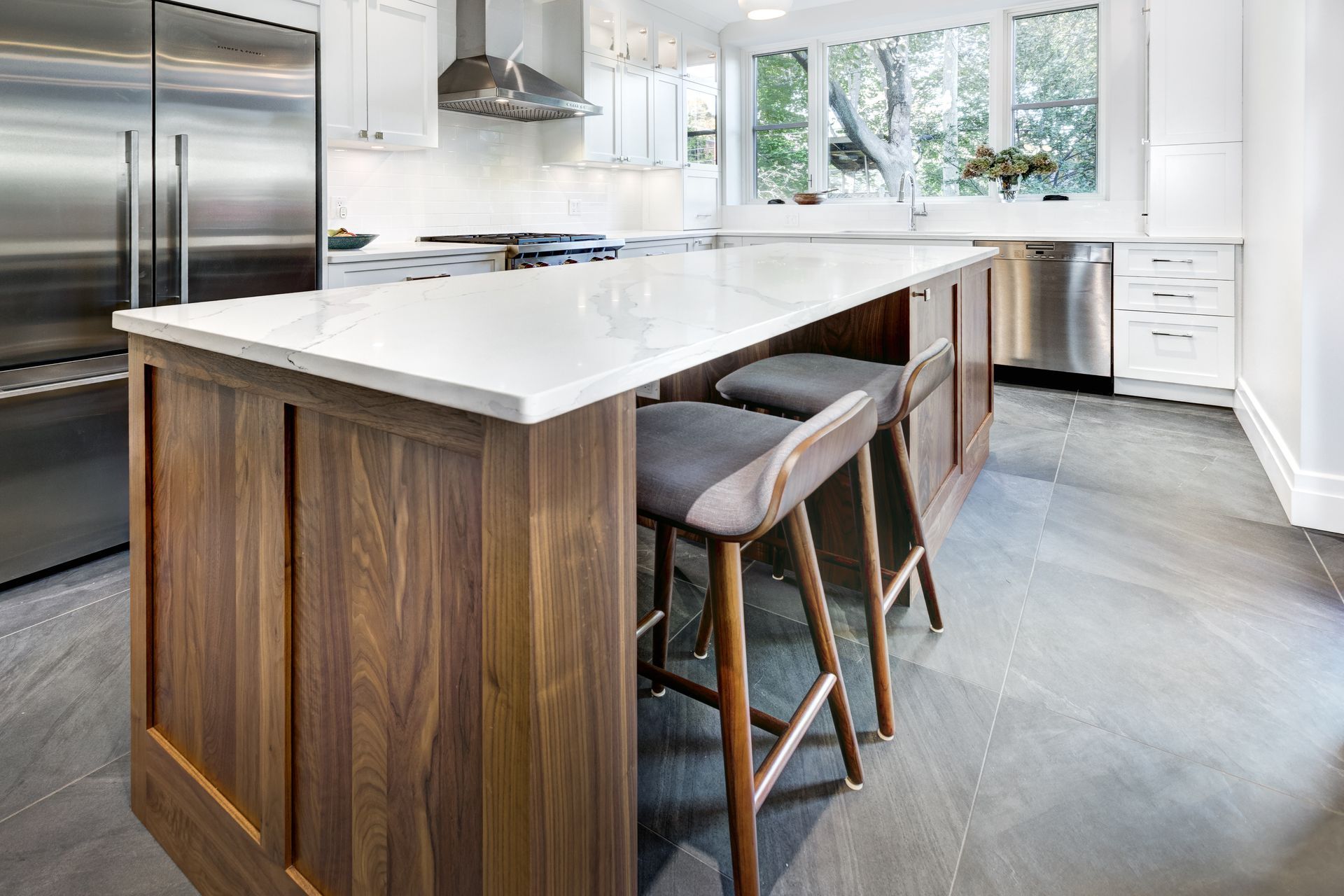Modern kitchen with a wooden island, two stools, white countertop, and stainless steel appliances.