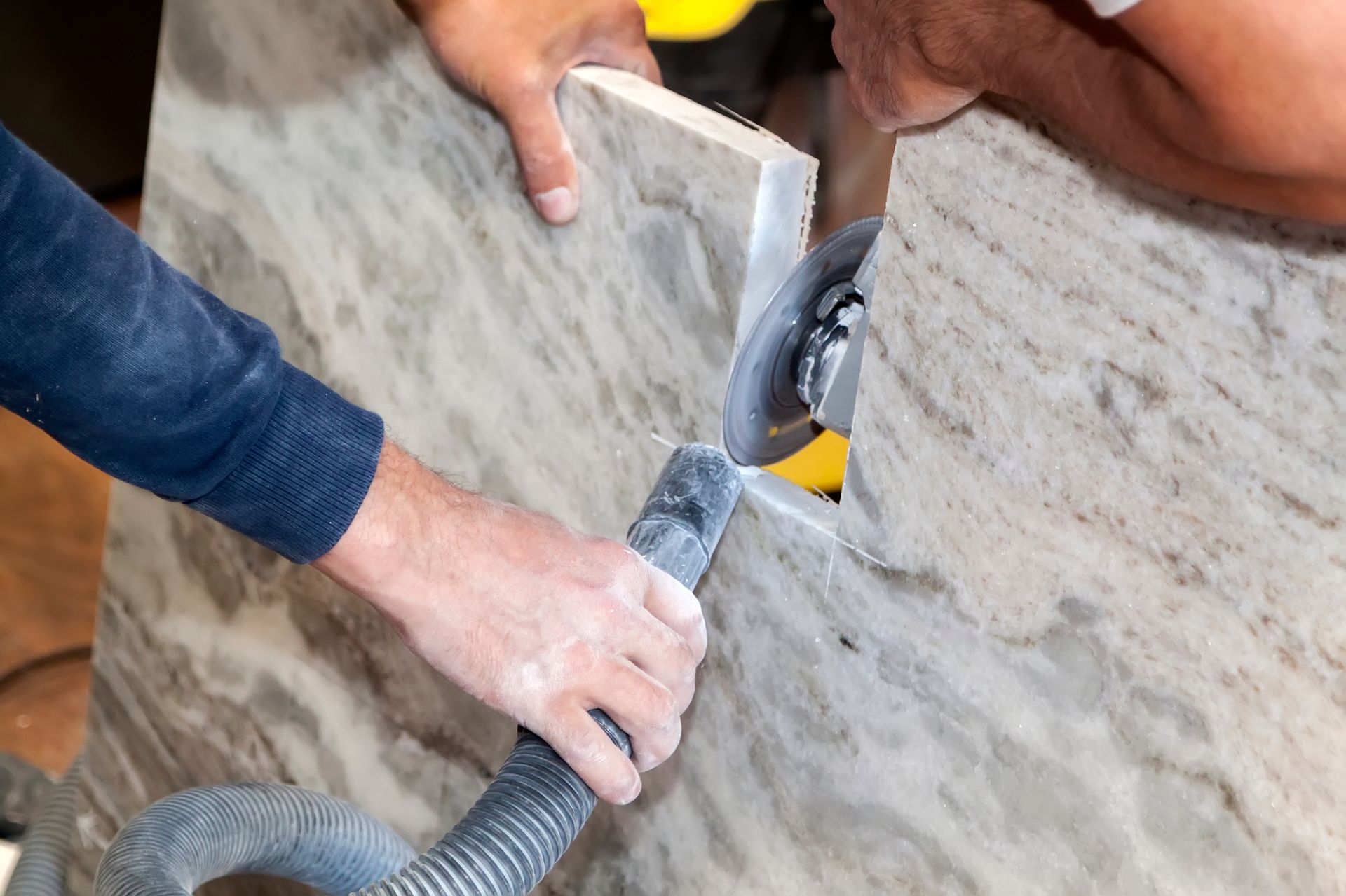 Two people cutting stone countertop with a power saw, using a vacuum to collect dust.