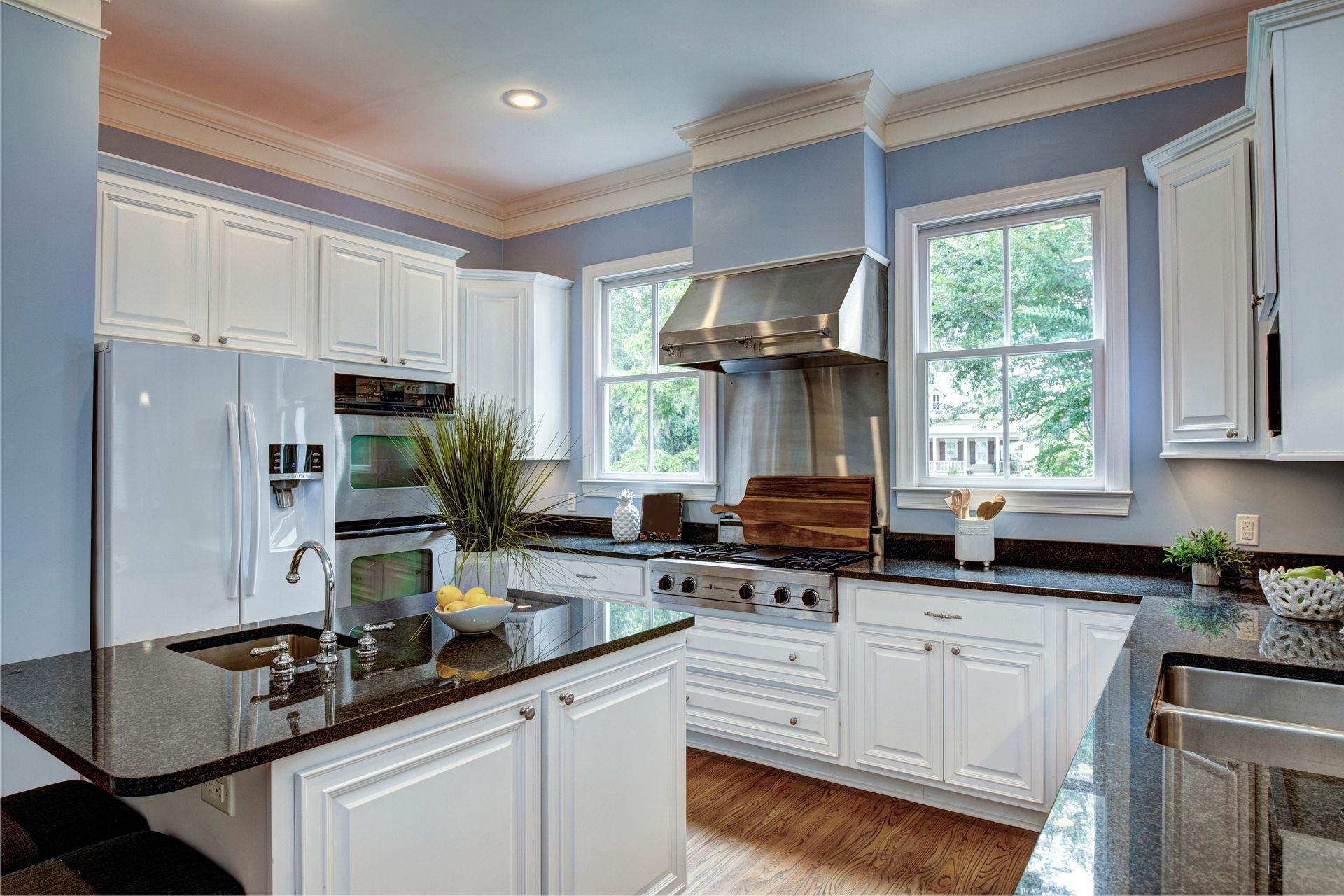 White kitchen with black countertops, blue walls, and stainless steel range hood.