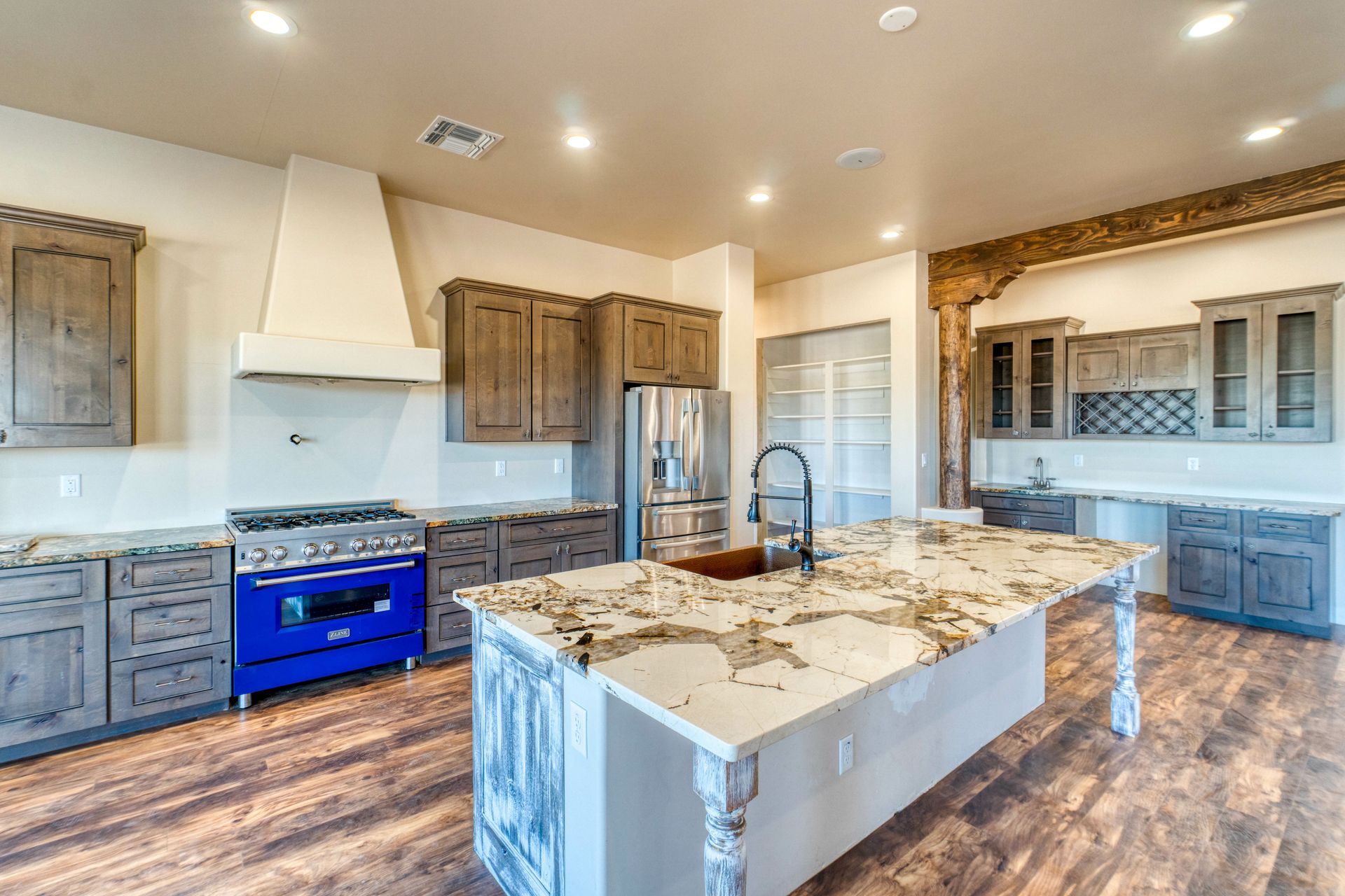 Spacious kitchen with rustic cabinets, blue stove, and granite island on wood flooring.