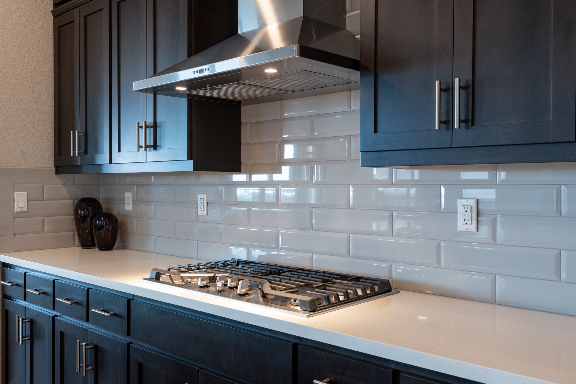 Black kitchen with gas cooktop, white countertops, gray subway tile backsplash, and dark cabinets.