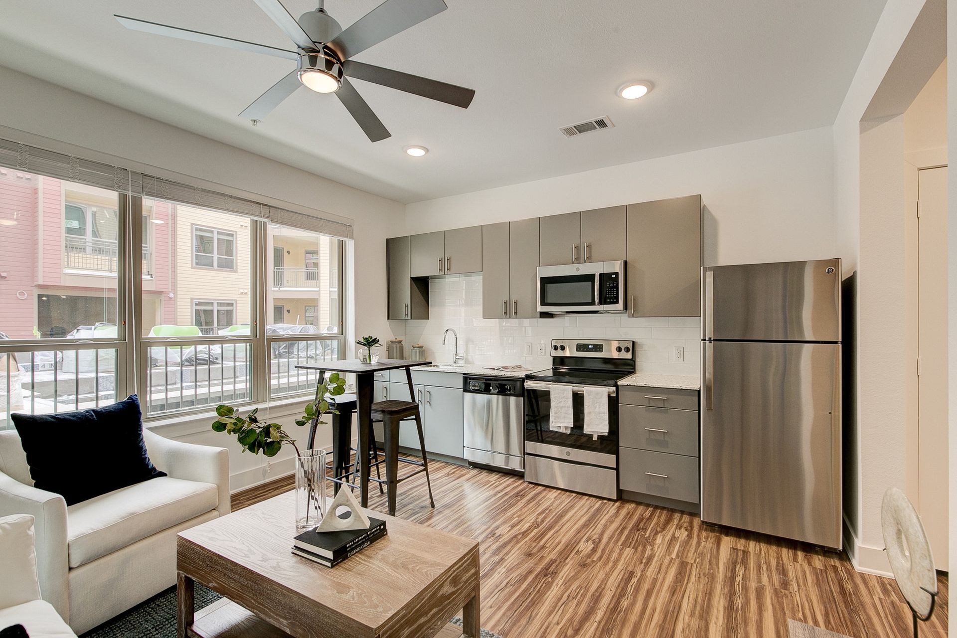 A living room with a ceiling fan and a kitchen with stainless steel appliances.