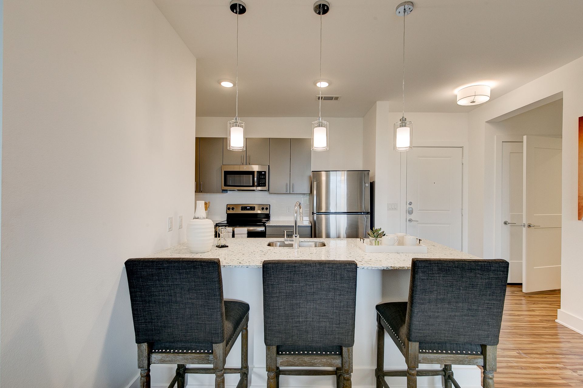 A kitchen with stainless steel appliances and a bar with three chairs.