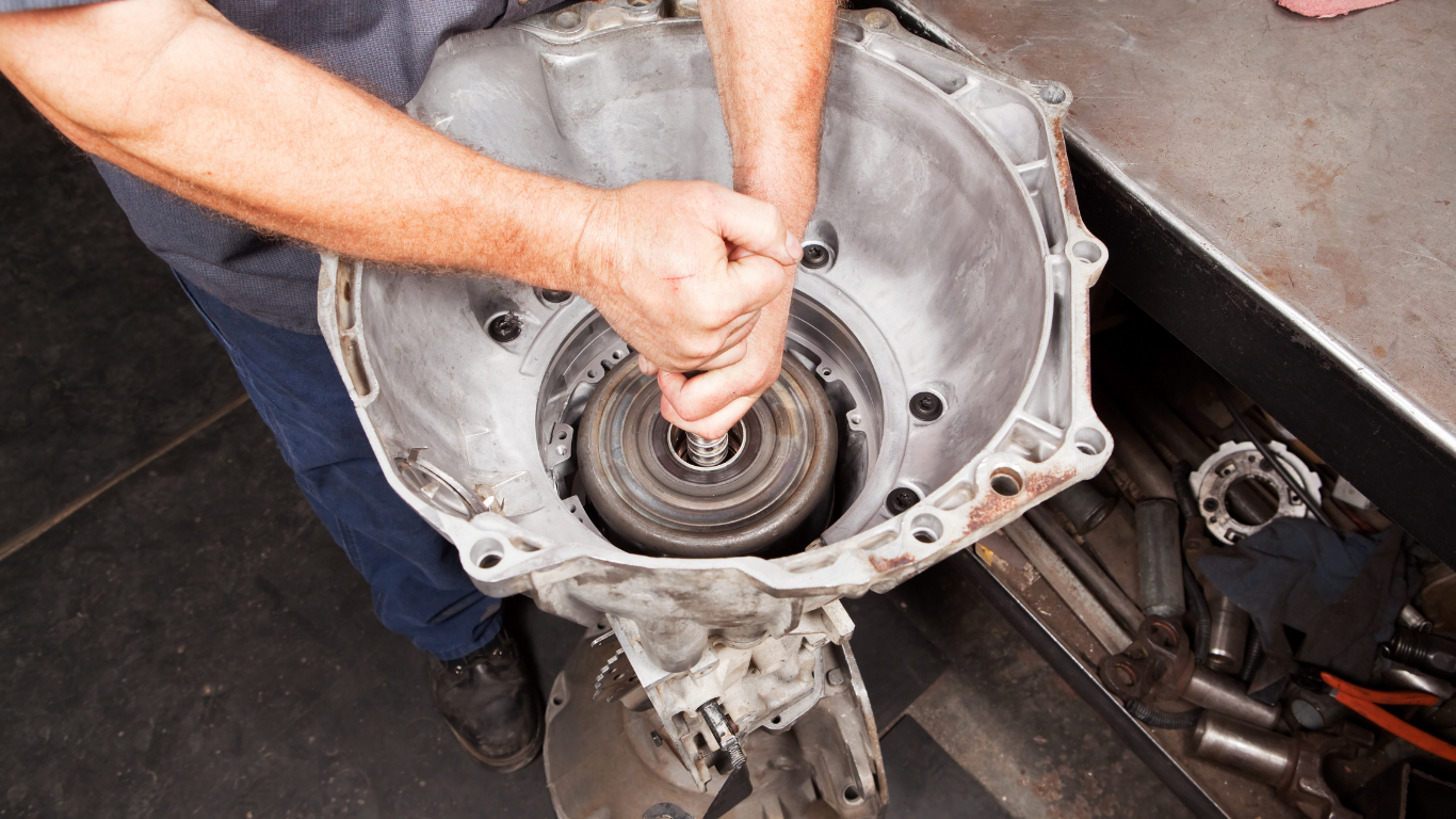 A man is working on a car transmission in a garage.