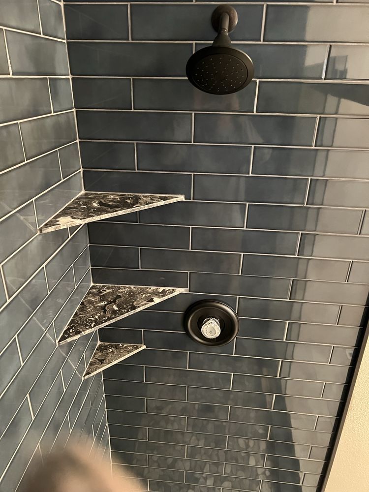Blue tiled shower with black showerhead, shelves, and water controls.