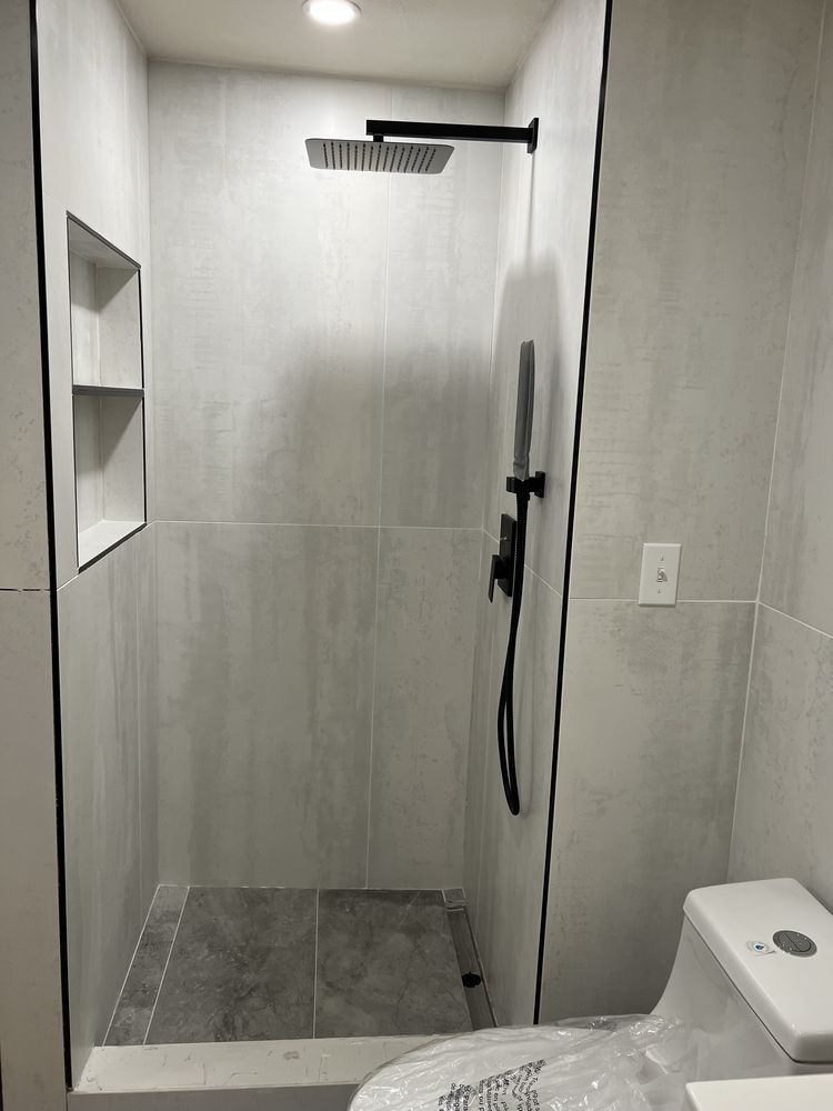 Shower with gray tiled walls, black fixtures, and toilet.