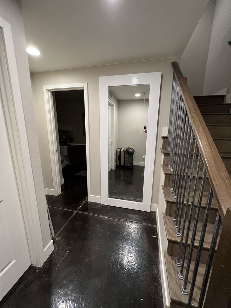 Hallway with a large mirror, stairs, and dark floor. White walls and door frames.