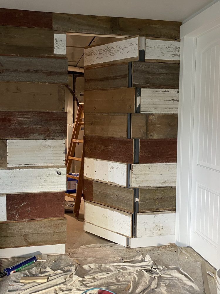 Room under construction, with reclaimed wood accent wall framing a doorway and white door on the right.