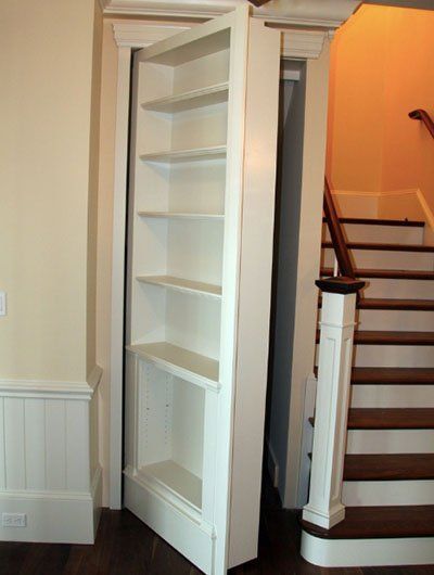 White bookshelf door open to reveal a staircase. Beige walls, wood floors, and steps.