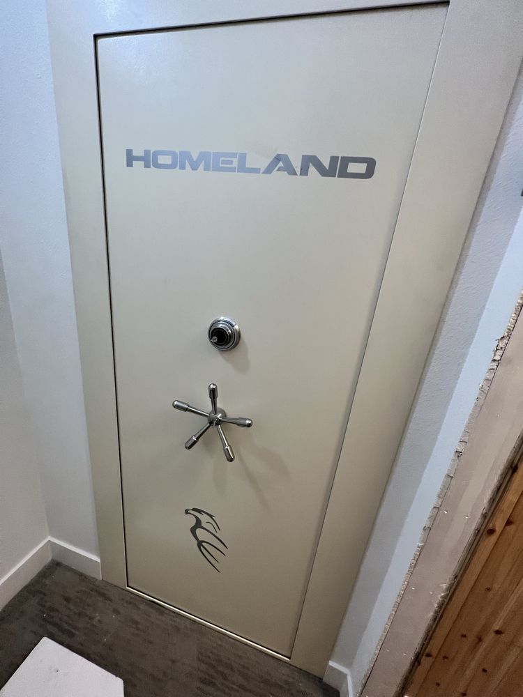A beige Homeland security door with a combination lock, star handle, and logo, built into a wall.