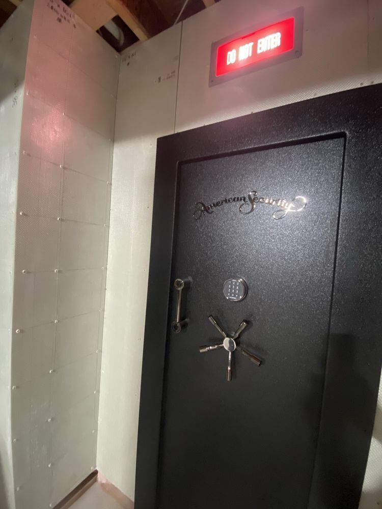 Black gun safe door with combination dial and handle, in a white-walled room with a red light above.