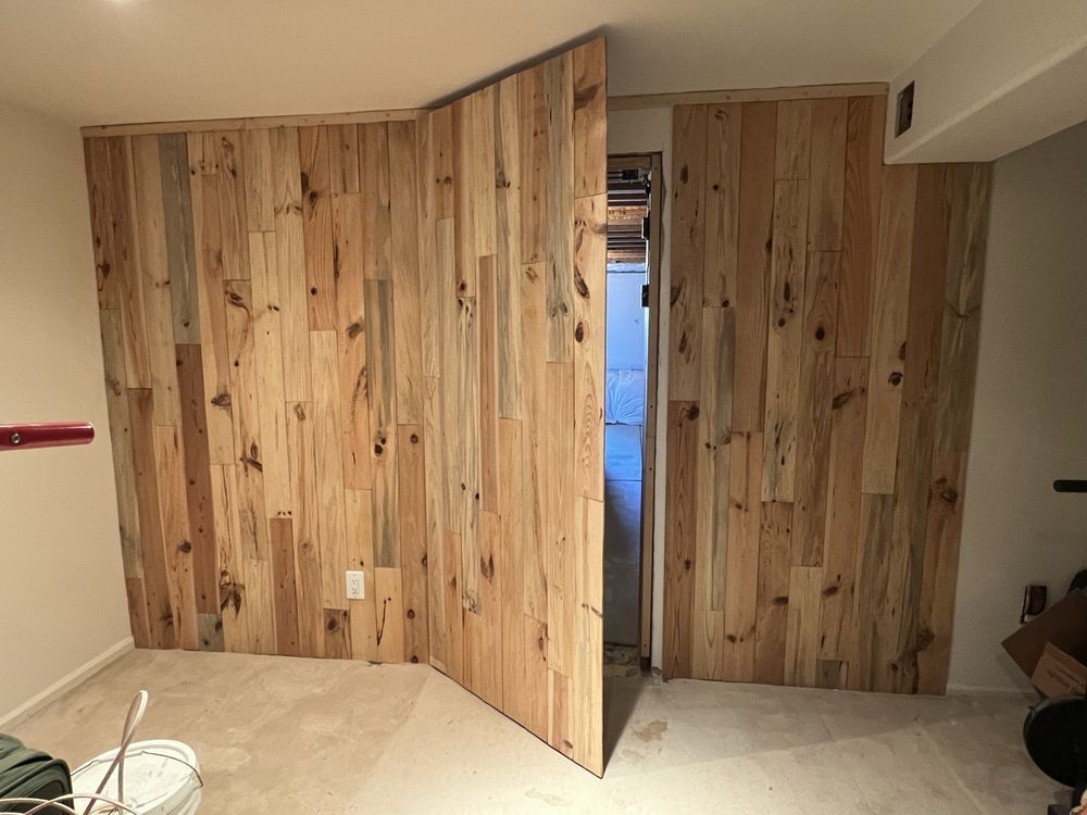 Wood-paneled walls with a doorway. One wall section is open. Interior space with carpet and a ceiling beam.